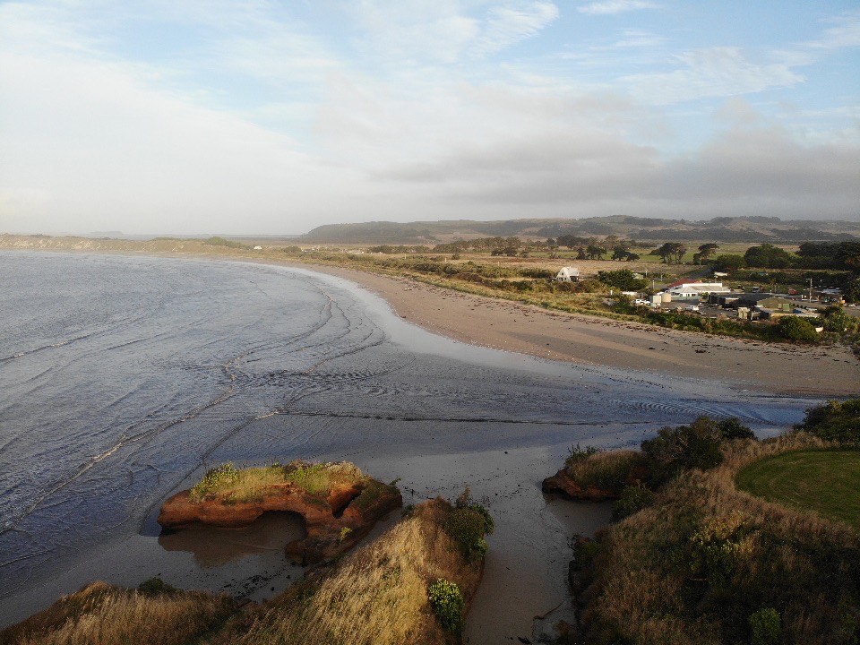 A river on the right runs out into a harbour mouth, with a few rural houses nearby.